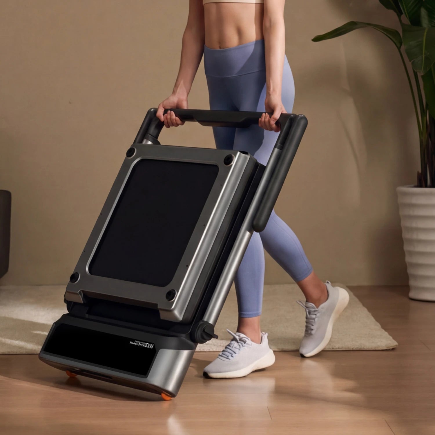 Woman easily moving folded MX3 treadmill using built-in wheels, showcasing effortless repositioning for home use.
