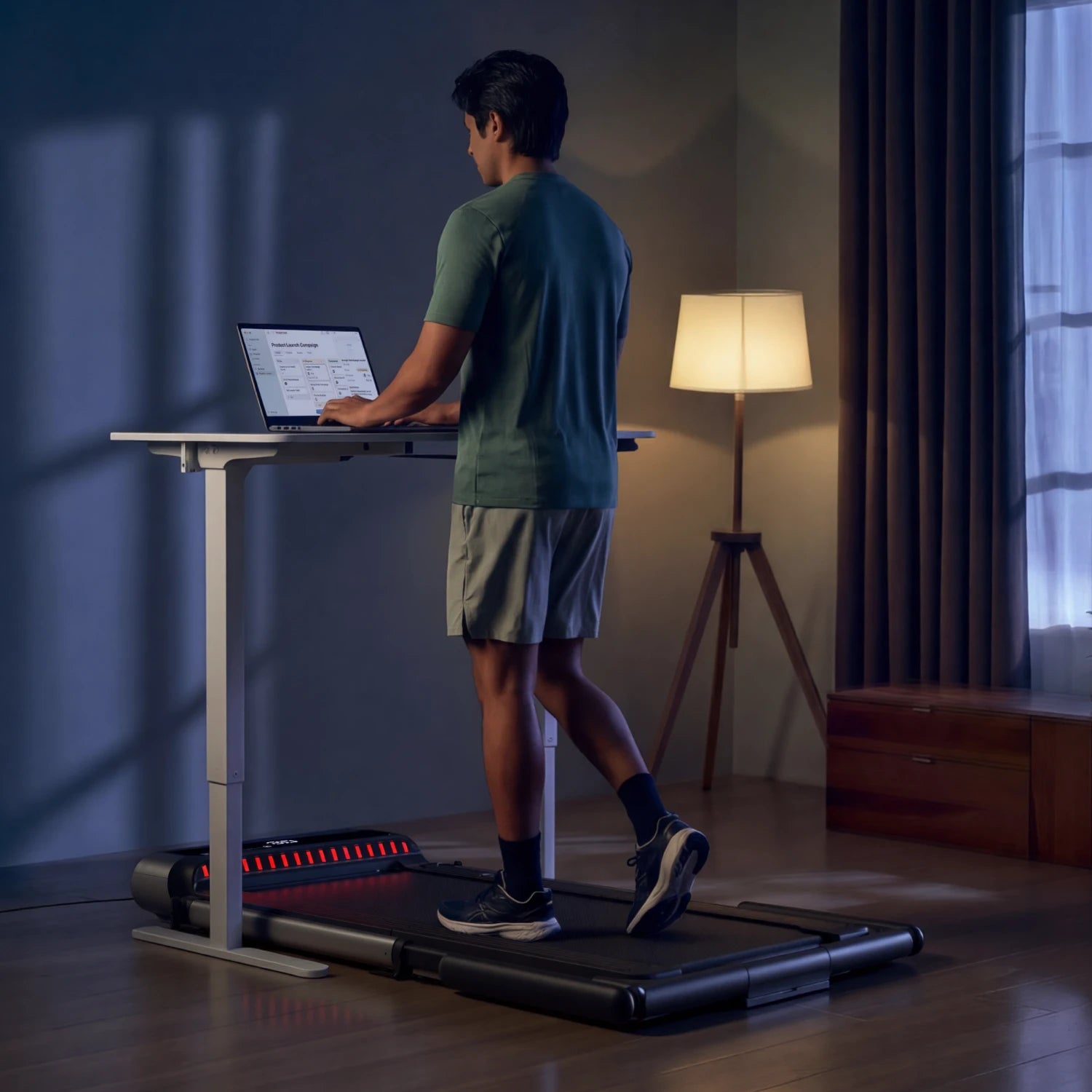 Man using MX3 treadmill under a standing desk at night, highlighting quiet operation for work.