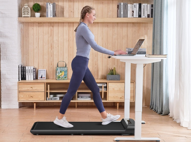 Walking on a compact under-desk treadmill while working on a laptop at a standing desk in a home office setting