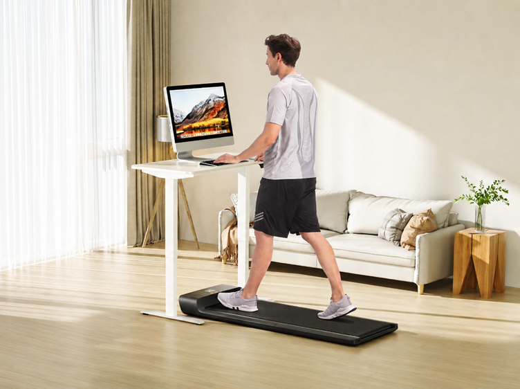 Man walking on a compact treadmill while working at a standing desk in a bright modern home office